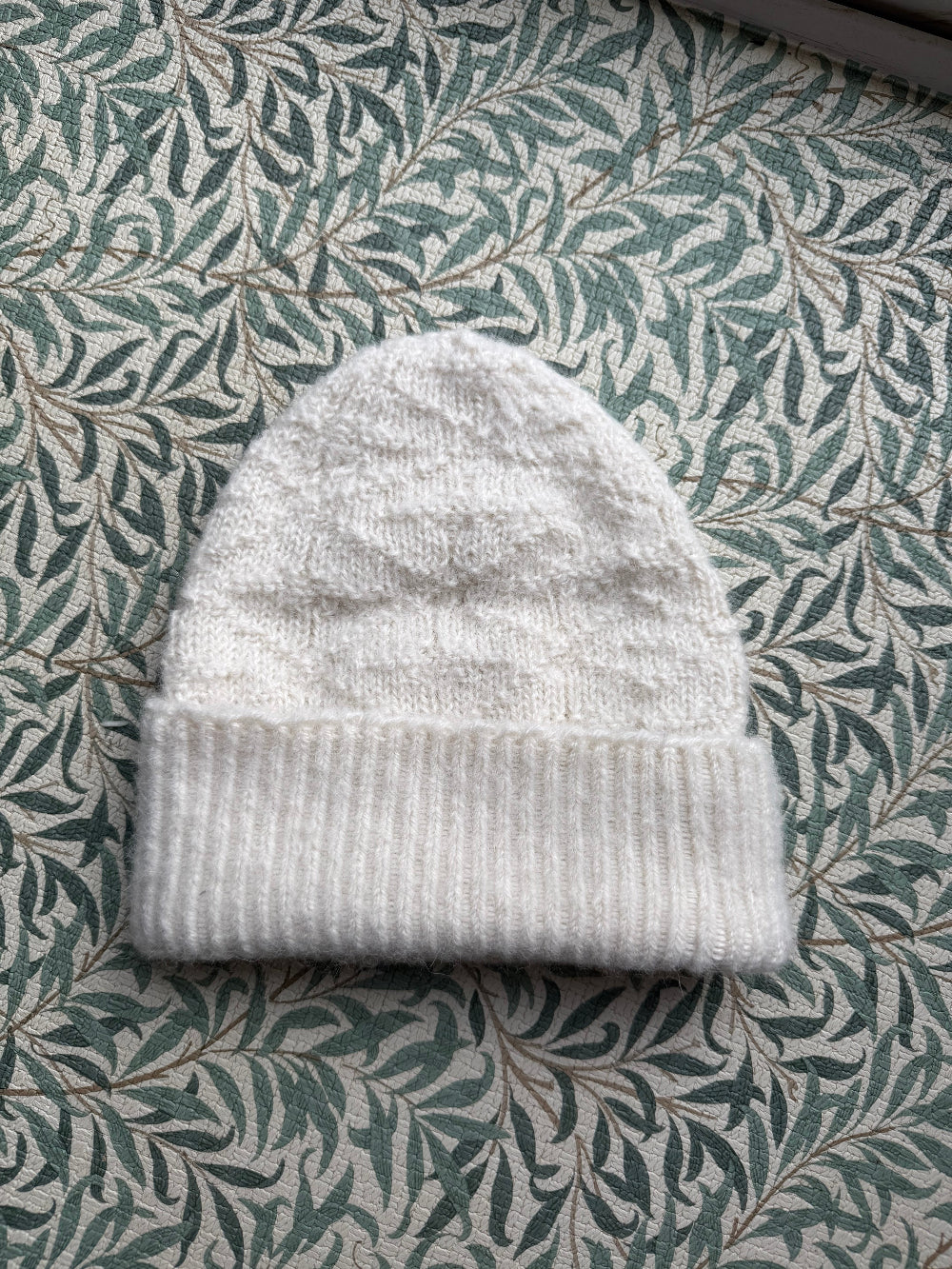 White knit alpaca wool beanie on a green leaf-patterned background
