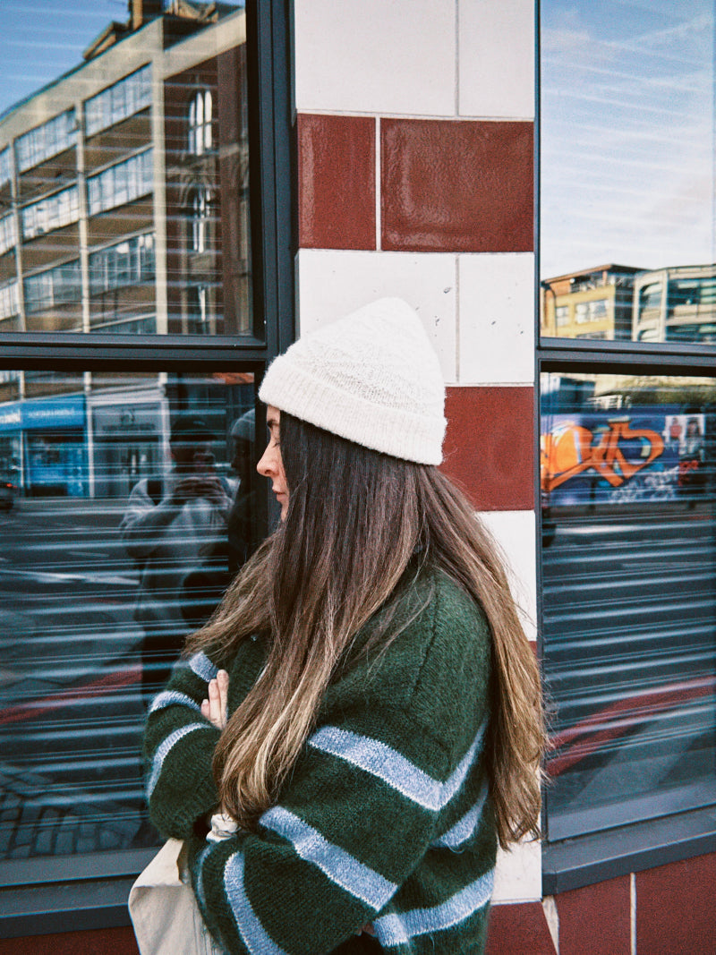 Woman wearing a white alpaca wool beanie and green striped cardigan.