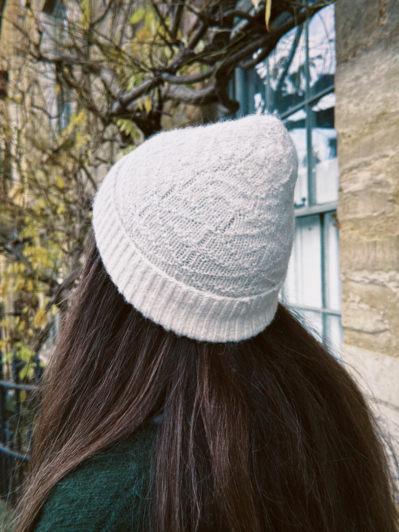 Person wearing a white knit alpaca wool beanie with stone background