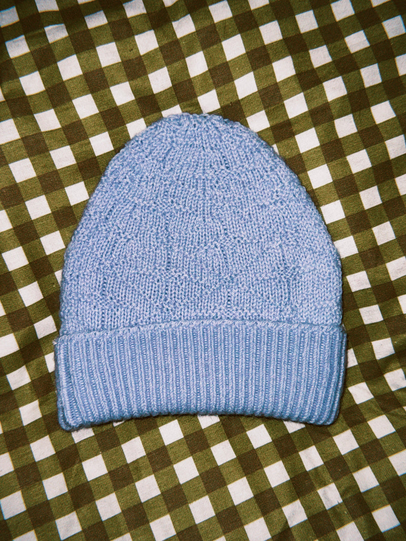 Blue knitted alpaca wool beanie on a green and white checkered background