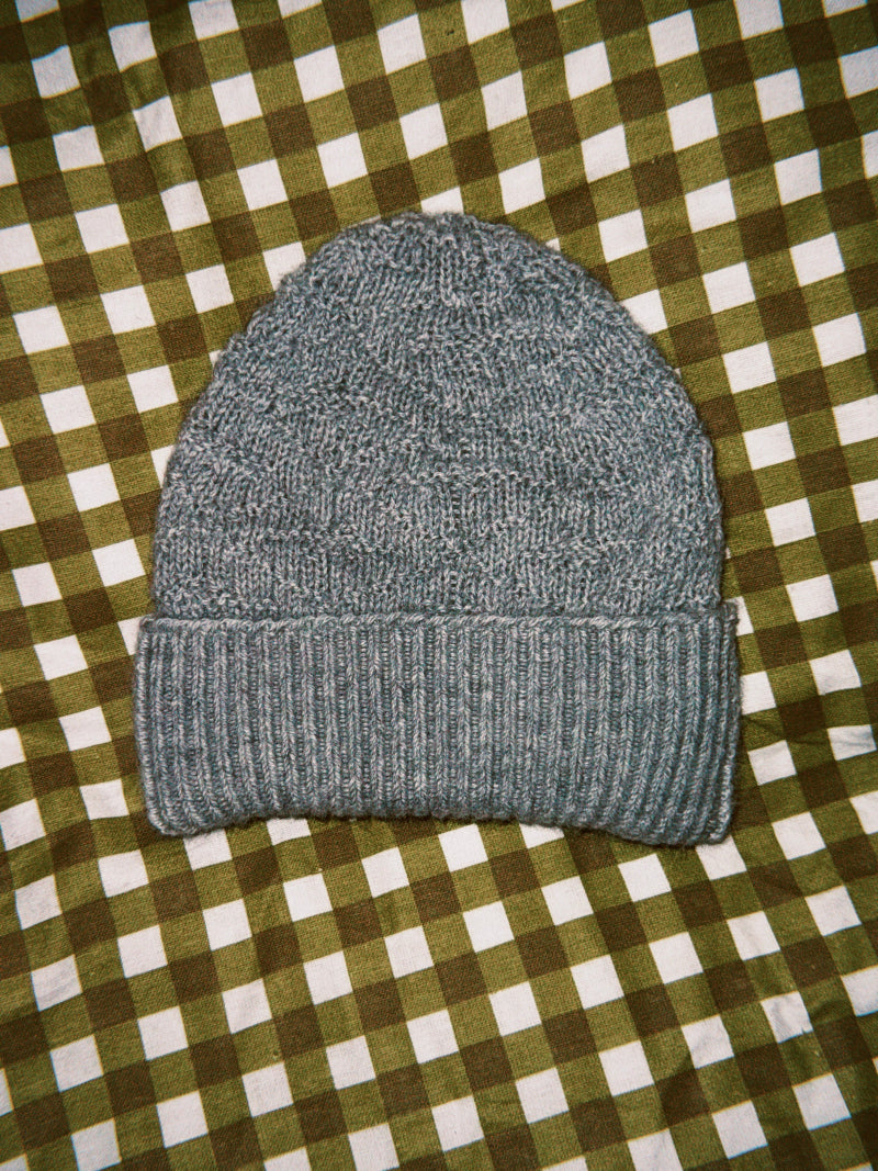 Gray knit alpaca wool beanie on a green and white checkered fabric background