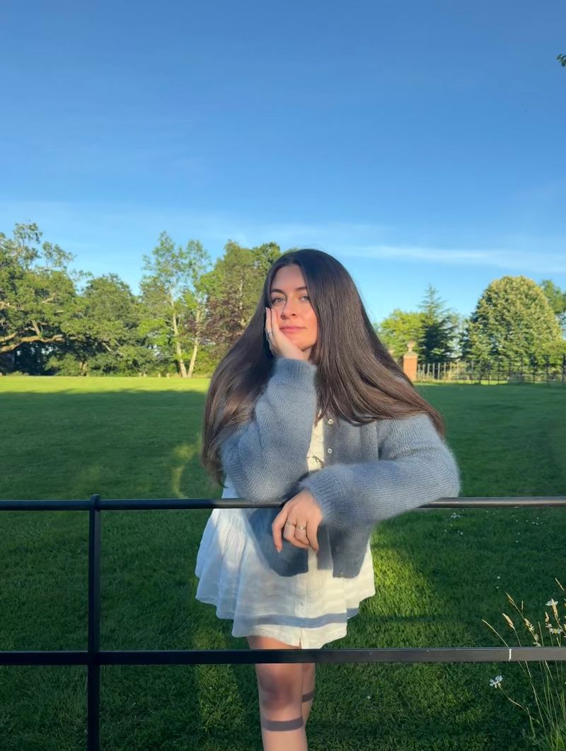 Woman standing outdoors in a blue mohair cardigan with green grass and trees.