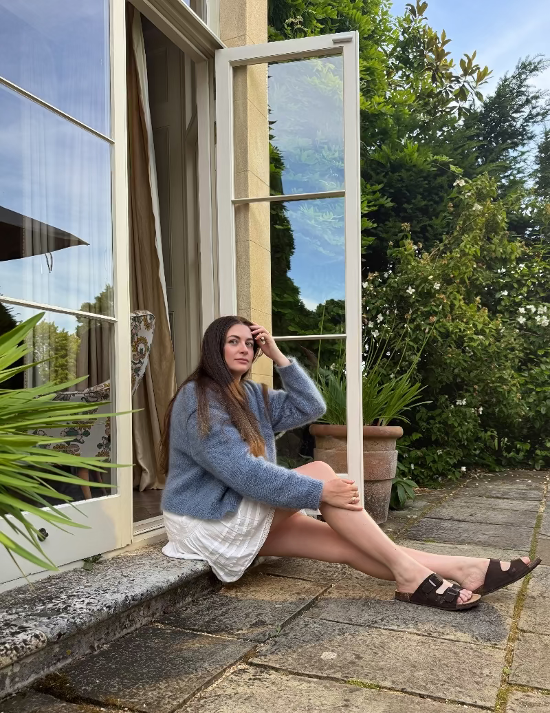 Woman sitting by a window with a garden view in a blue mohair cardigan.