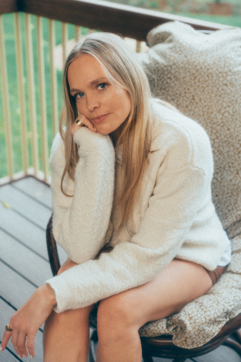 Woman in a Cream alpaca wool cardigan sitting on a textured chair outdoors.
