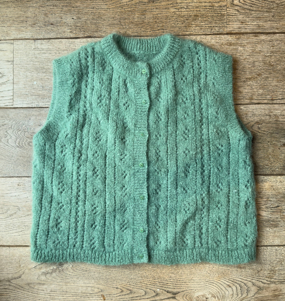 Green knitted mohair pointelle vest on a wooden surface